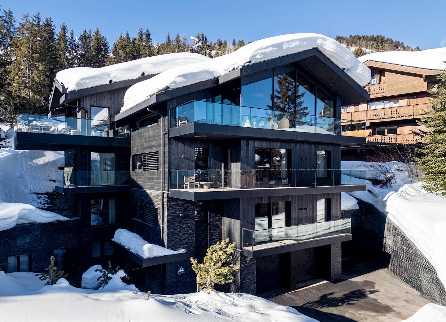 Modern donker chalet in Courchevel 1850 met glazen balkons en besneeuwde daken op een zonnige dag